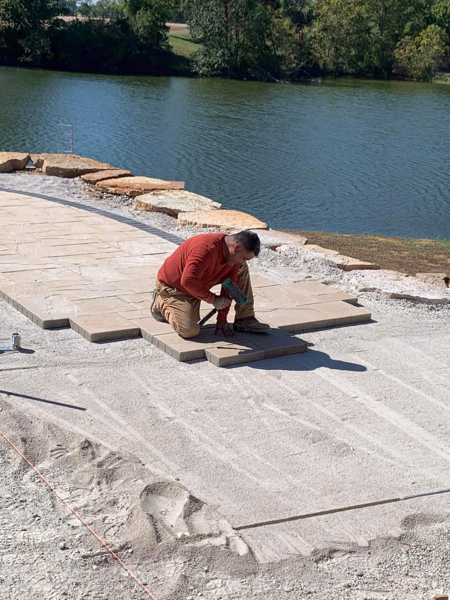 Tapping a paver into place on a prepared base beside the pool
