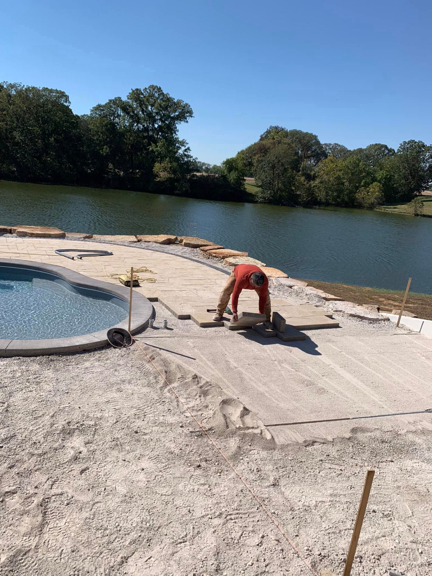 Setting large stone pavers along a poolside patio beside a lake